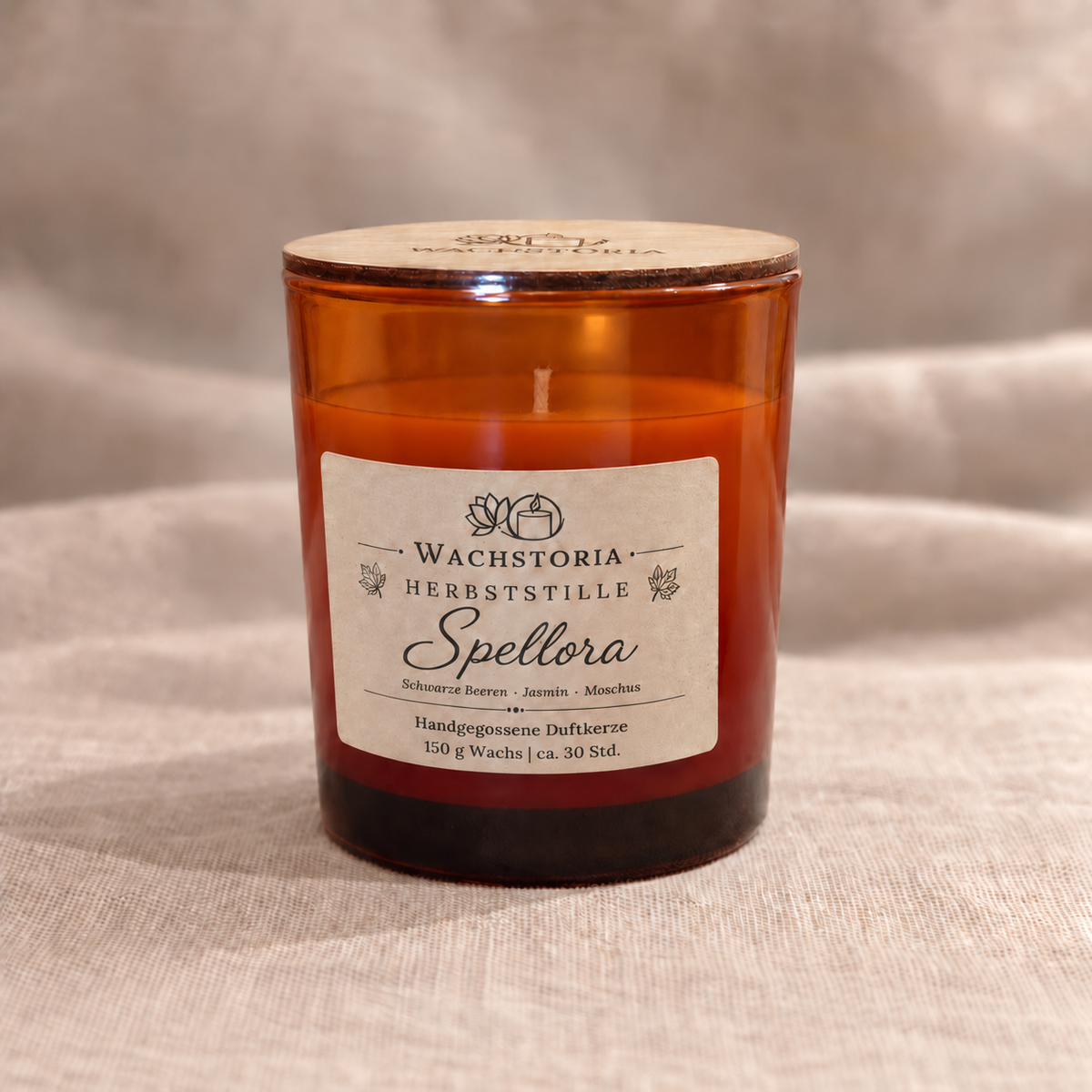 Wachstoria Duftkerze Spellora, 150 g, im bernsteinfarbenen Glas mit dünnem Holzdeckel und Kraftpapieretikett auf beigem Leinen.